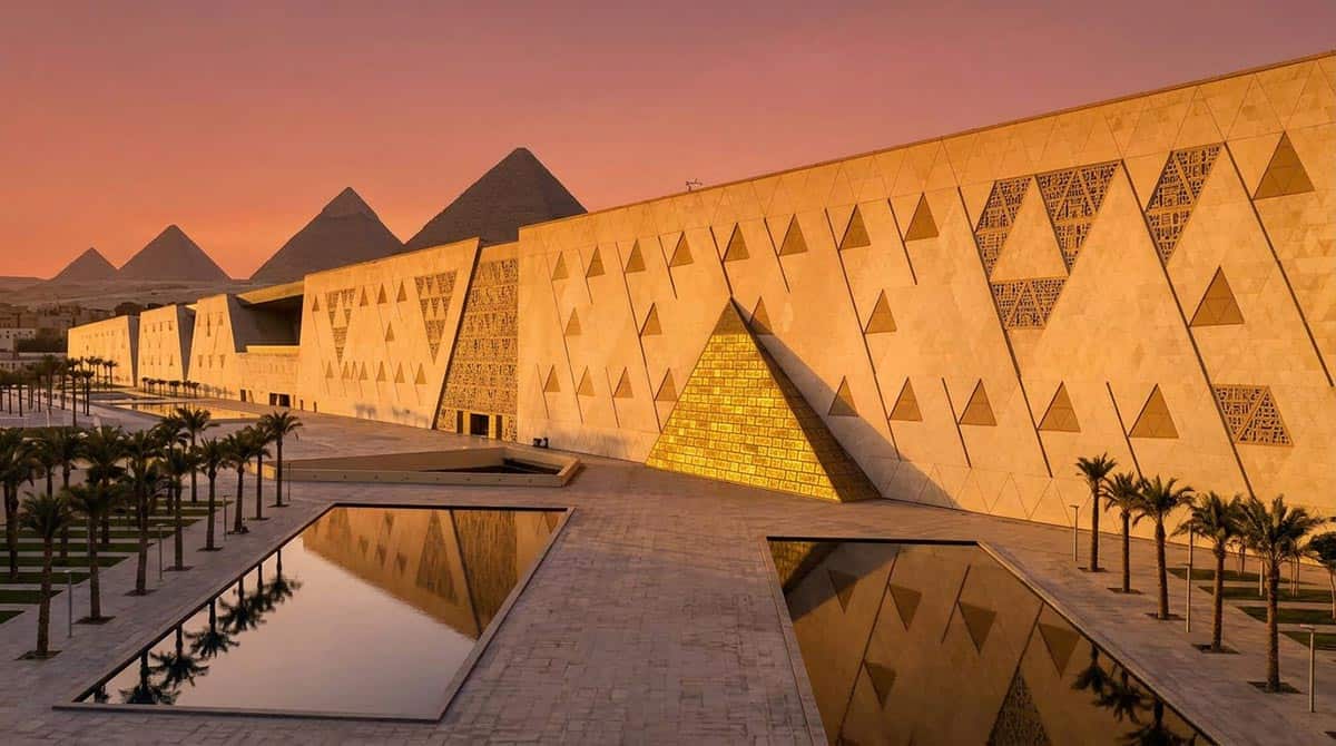 Grand Egyptian Museum glowing gold at sunset with the Great Pyramids of Giza silhouetted in the background